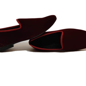 May include: A pair of burgundy velvet loafers with red trim. The shoes have a classic slip-on design with a rounded toe and a low heel. The interior is black.