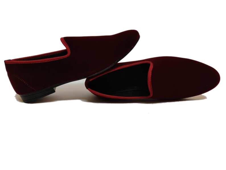 May include: A pair of burgundy velvet loafers with red trim. The shoes have a classic slip-on design with a rounded toe and a low heel. The interior is black.