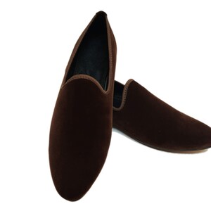 May include: A pair of brown velvet loafers. The loafers are pointed-toe and have a slip-on design.