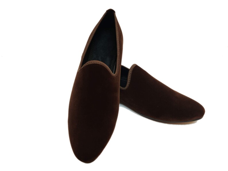 May include: A pair of brown velvet loafers. The loafers are pointed-toe and have a slip-on design.