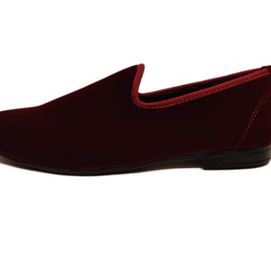 May include: A burgundy velvet loafer with a rounded toe and a low heel. The shoe has a red trim around the opening and a black sole. The shoe is a slip-on style.