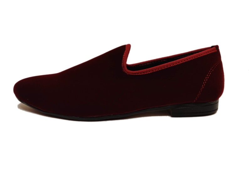 May include: A burgundy velvet loafer with a rounded toe and a low heel. The shoe has a red trim around the opening and a black sole. The shoe is a slip-on style.