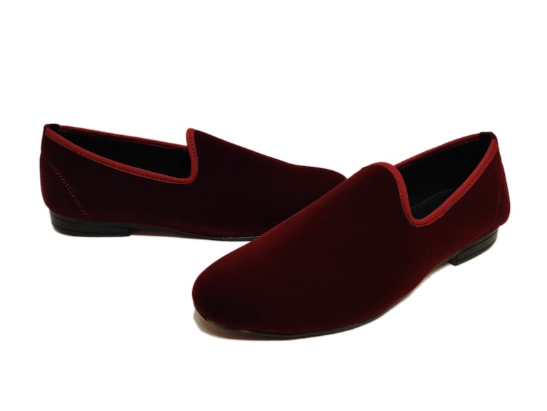 May include: Burgundy velvet loafers. These slip-on shoes have a rounded toe and a contrasting red trim around the opening. The soles are black. The shoes are a classic style.