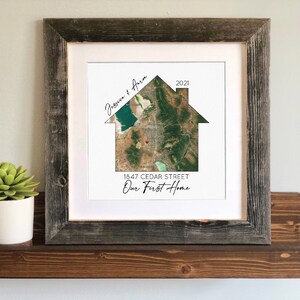 May include: A framed print with a house-shaped map of a neighborhood. The map is in shades of green and brown with a red heart marking a location. The text on the print reads "Jess and Aaron 2021 1847 Cedar Street Our First Home".