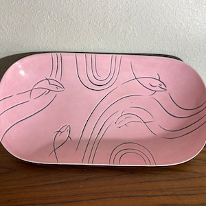 May include: A pink ceramic serving dish with a black and white design of stylized fish swimming in waves.