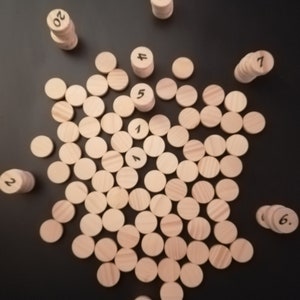 Puede incluir: Un conjunto de contadores de n&uacute;meros de madera, con los n&uacute;meros del 1 al 20, dispuestos sobre una superficie negra. Los contadores est&aacute;n apilados en pilas, con el n&uacute;mero hacia arriba.