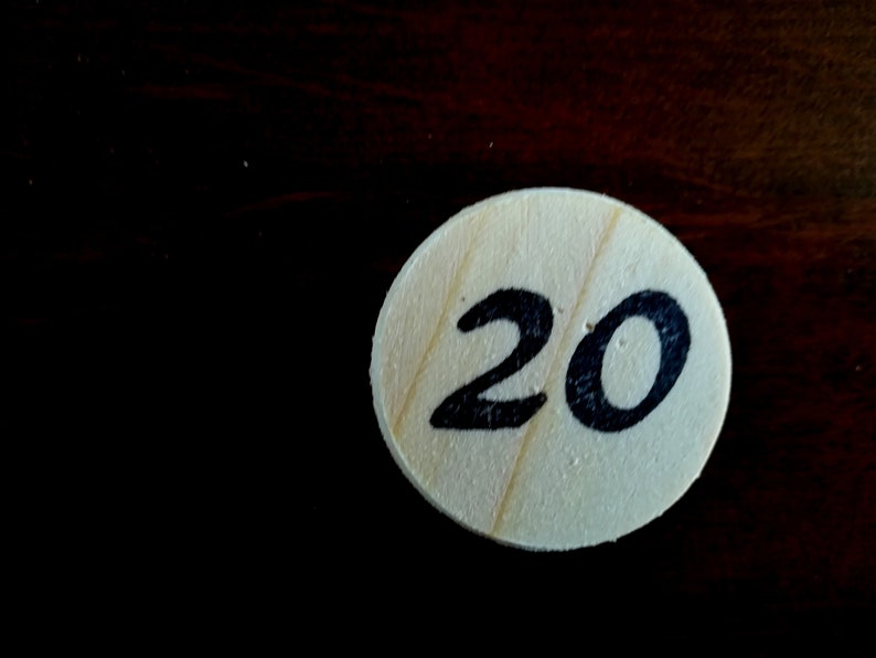 Puede incluir: Una ficha redonda de madera con el n&uacute;mero 20 escrito en tinta negra.