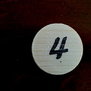 Puede incluir: Una ficha redonda de madera con el n&uacute;mero "4" escrito en tinta negra.