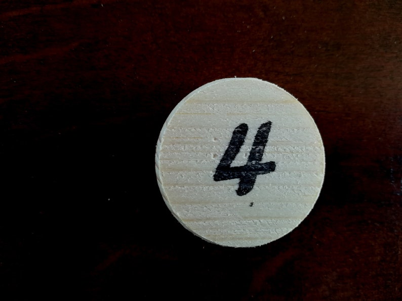 Puede incluir: Una ficha redonda de madera con el n&uacute;mero "4" escrito en tinta negra.