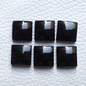 May include: Six individual square-shaped black cabochons with a smooth, polished, and reflective surface. Each piece features a flat base and a slightly domed top, displaying a deep, solid black colour with bright white light reflections on the surface.
