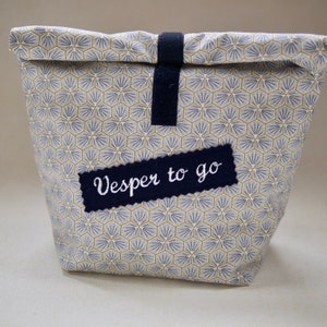 May include: A white fabric bag with a geometric pattern in shades of gray and gold. The bag has a black strap and a label that says "Vesper to go".