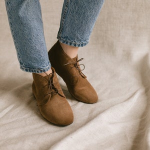 May include: Brown suede ankle boots with laces. The boots are worn with blue jeans.