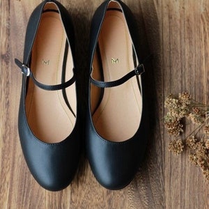 May include: A pair of black leather ballet flats with a strap across the top. The strap has a small gold buckle. The shoes have a rounded toe.