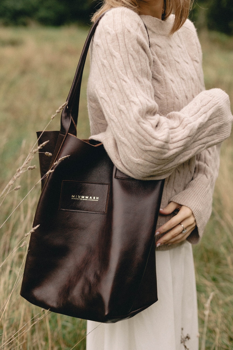 May include: A brown leather tote bag with a gold logo that reads "NIUMMASH HANDCRAFTED BAGS & ACCESSORIES".