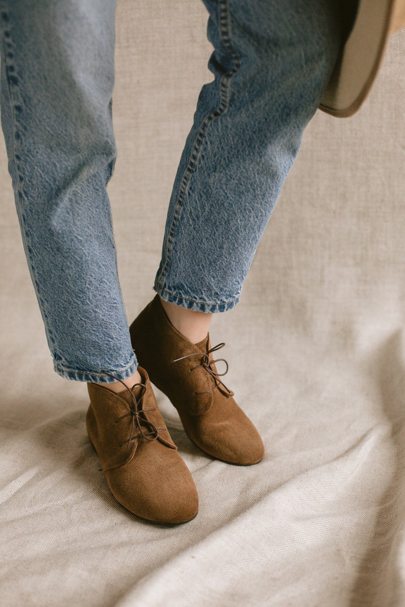 May include: Brown suede ankle boots with laces. The boots are worn with blue jeans.