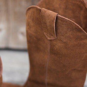 K&ouml;nnte beinhalten: Braune Wildleder-Cowgirl-Stiefel mit spitzer Zehenpartie und einem Zuglaschen am R&uuml;cken.