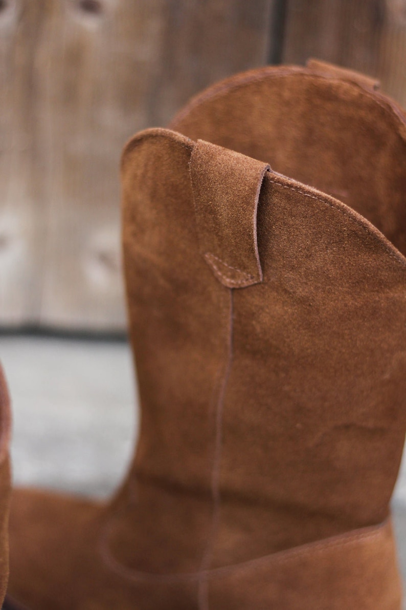 K&ouml;nnte beinhalten: Braune Wildleder-Cowgirl-Stiefel mit spitzer Zehenpartie und einem Zuglaschen am R&uuml;cken.