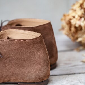 May include: A pair of brown suede ankle boots with a lace-up closure. The boots are shown from the back, with the laces and the back of the heel visible.