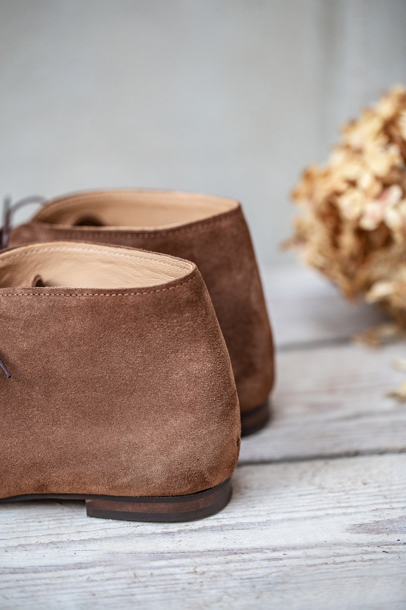 May include: A pair of brown suede ankle boots with a lace-up closure. The boots are shown from the back, with the laces and the back of the heel visible.