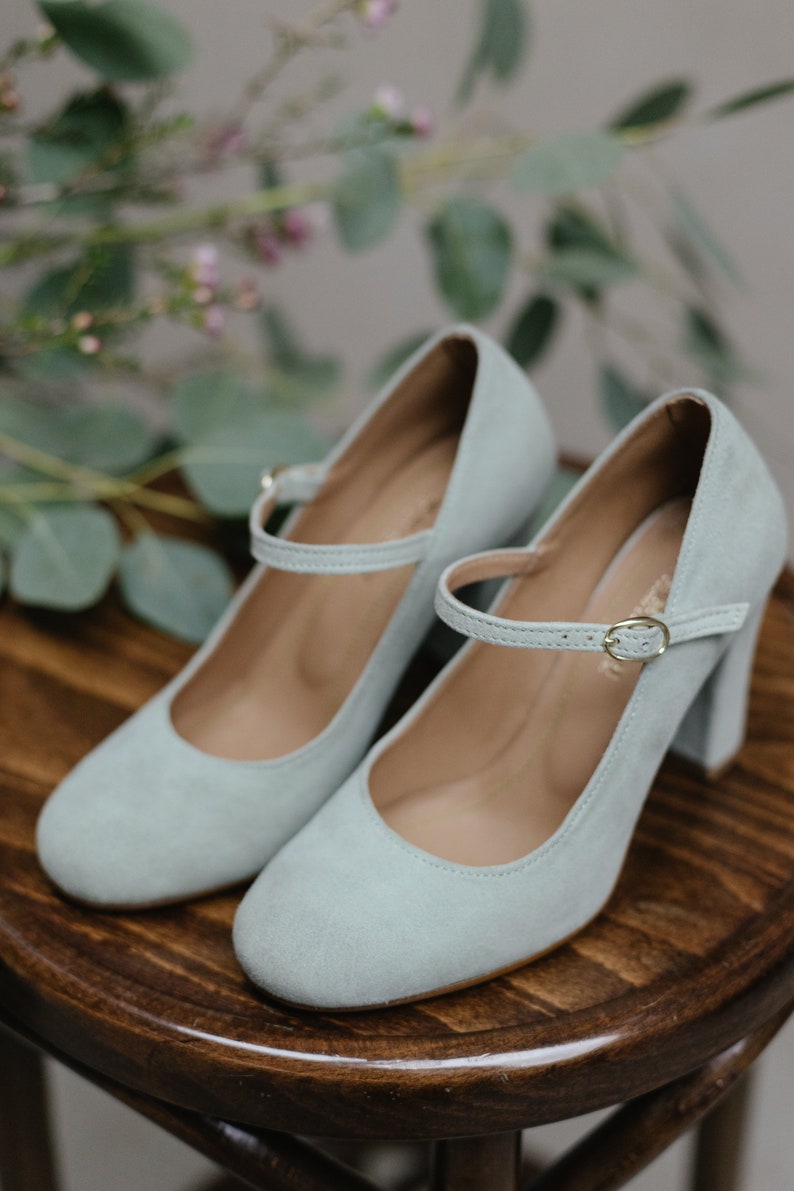May include: A pair of light blue suede heeled shoes with a buckle strap. The shoes have a block heel and a rounded toe.