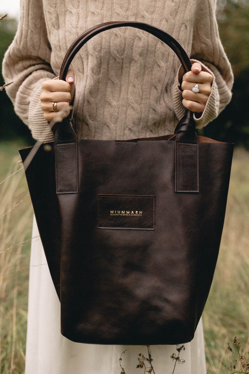 May include: A brown leather tote bag with a gold logo that reads "MIUMMASH handcrafted leather & accessories".