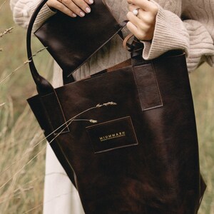 May include: A brown leather tote bag with a smaller brown leather pouch inside. The tote bag has a gold logo that reads "MIUMMASH Handmade Goods & Accessories".