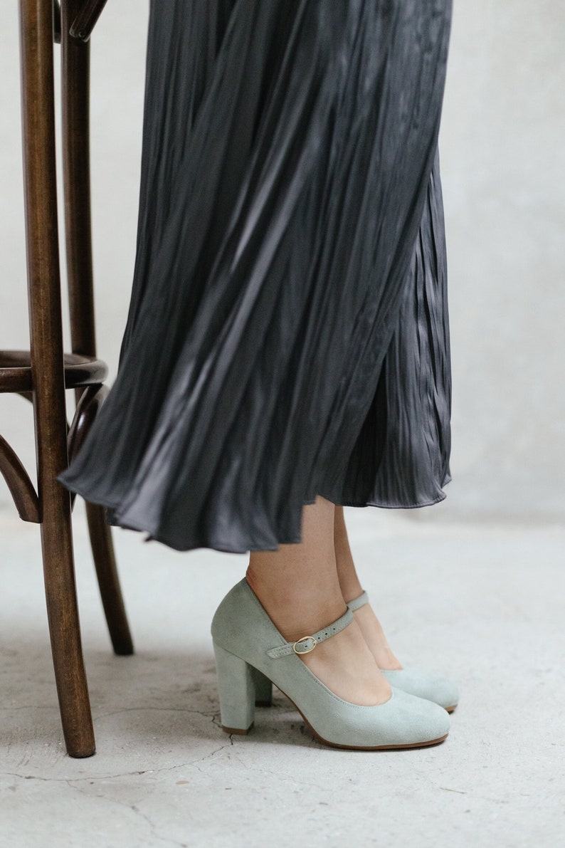 May include: A pair of light blue suede heeled shoes with a buckle strap. The shoes have a chunky heel and a rounded toe.