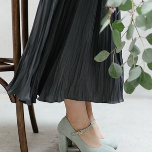 May include: A pair of light blue suede heeled shoes with a buckle strap. The shoes have a chunky heel and a rounded toe.