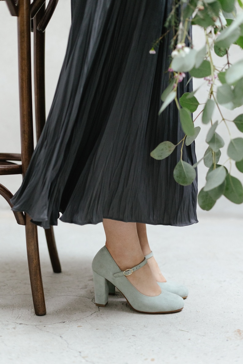 May include: A pair of light blue suede heeled shoes with a buckle strap. The shoes have a chunky heel and a rounded toe.