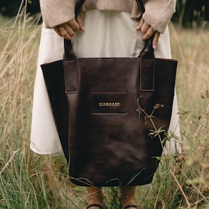 May include: A brown leather tote bag with a gold logo that reads "MIUMMASH" in a field of tall grass.