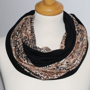 Puede incluir: Una bufanda infinita negra y marrón con estampado de leopardo.