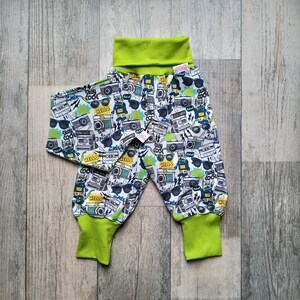 Puede incluir: Pantalones de bebé verde y blanco con un estampado de cámaras, gafas de sol y las palabras "Stay Cool" y "Hello".