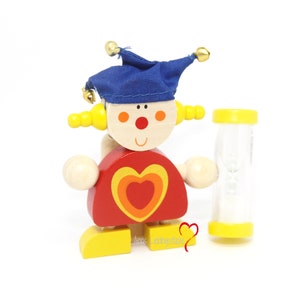 May include: A wooden toy clown with a blue hat, yellow hair, and a red heart on its chest. The clown is holding a yellow hourglass.