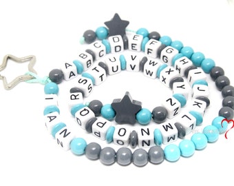 Könnte beinhalten: Eine blaue und graue Alphabet-Perlenkette mit einem Sternanhänger. Die Kette besteht aus Holzperlen mit aufgedruckten Buchstaben. Die Perlen sind auf einer weißen Schnur aufgefädelt.