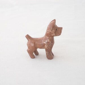 May include: A small, brown wooden dog figurine. The dog is standing on all four legs and has a simple, stylized design.