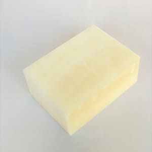 Puede incluir: Una barra de jabón rectangular blanca con un tono ligeramente amarillento. El jabón está sobre una superficie blanca.