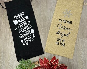 May include: Two wine bottle bags. One black bag has the text "CHRISTMAS CHEER STARTS RIGHT HERE" in white. The other bag is tan with the text "IT'S THE MOST Wine-derful TIME OF THE YEAR" in black.
