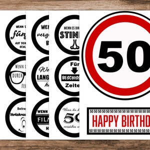 May include: A set of nine black and white round stickers with various sayings in German. The stickers are designed to look like traffic signs. The stickers are arranged in three rows of three. The top row says "WENN T" "f&uuml;n" "AUF DEN" "SCHL" "WEI" "verg" "B". The middle row says "WENN D" "DURCH" "FEI" "We" "LANG" "50" "BESCHISS" "Zeite". The bottom row says "Beitra" "Verkelurssi" "WENN" "FILA" "Wenn du d" "50" "vers&uuml;ben w" "H". The stickers are surrounded by a white border. Below the stickers is a red banner with the text "HAPPY BIRTHDAY" in white letters. The banner is surrounded by a white border. The background is a wooden surface.