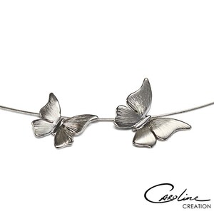 Puede incluir: Un collar de plata con dos colgantes de mariposa. Las mariposas se miran y est&aacute;n conectadas por una fina cadena de plata.