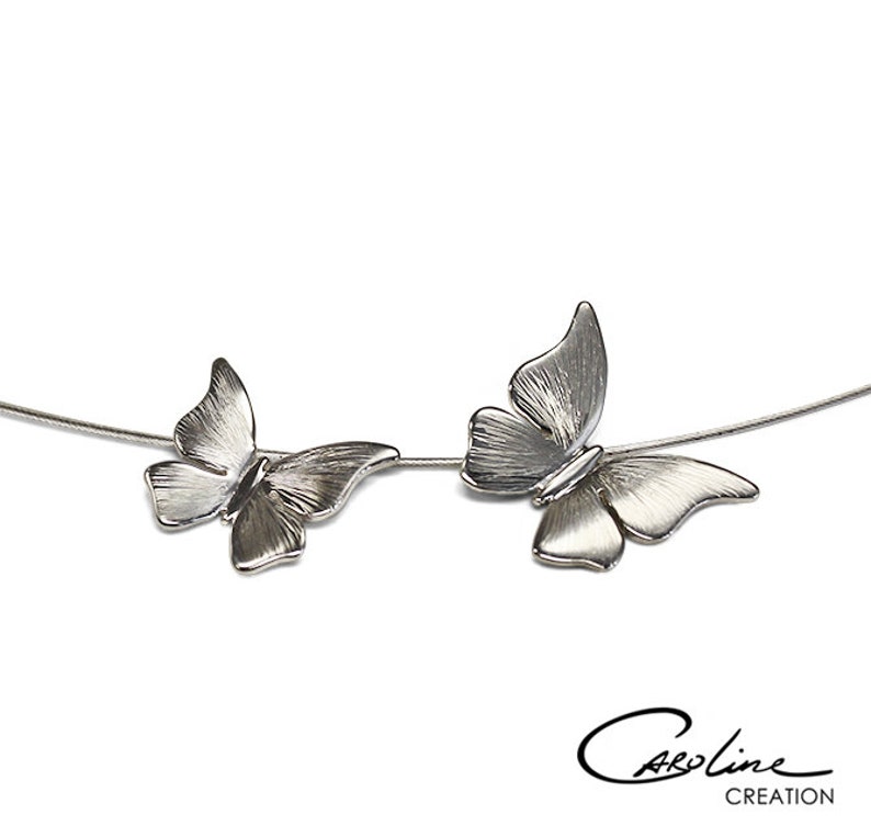 Puede incluir: Un collar de plata con dos colgantes de mariposa. Las mariposas se miran y est&aacute;n conectadas por una fina cadena de plata.