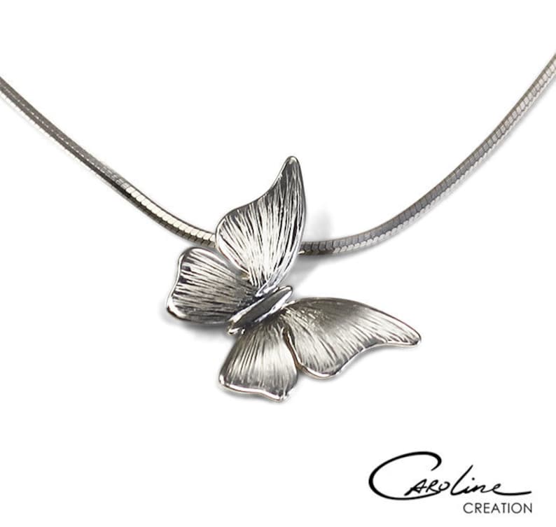 Puede incluir: Un collar de cadena de plata con un colgante de mariposa detallado. La mariposa es texturizada y tiene un dise&ntilde;o delicado.