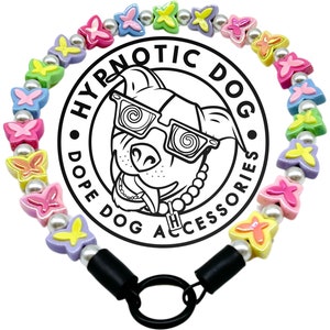 May include: A dog collar with butterfly-shaped beads in pastel shades, with pearl-like beads between them. The collar has black connectors and a black ring. The image includes a logo with a dog wearing glasses and the text "HYPNOTIC DOG ACCESSORIES."