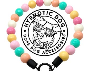 May include: A pet collar featuring a circular arrangement of smooth, multicolored beads in shades of pink, yellow, peach, and teal. The collar includes a black metal ring attachment and a central logo with a dog wearing glasses and the text HYPNOTIC DOG.