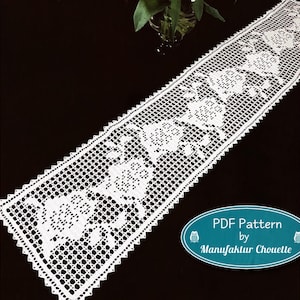 Pode incluir: Um caminho de mesa retangular de crochê branco com um padrão floral repetitivo e uma borda festonada. Uma etiqueta oval azul-petróleo no canto inferior direito exibe o texto: PDF Pattern by Manufaktur Chouette com dois pequenos ícones de coruja.