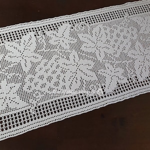 May include: White crocheted table runner with a floral design. The runner features a delicate lace pattern and the words "Merry Christmas" in a stylized font.