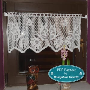 May include: A white, crocheted lace window valance with a floral design, suspended from a white rod. The valance features a scalloped lower edge. The image also shows a wooden owl ornament and a potted plant.