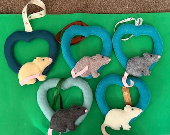 May include: Five felt heart-shaped ornaments in shades of blue and teal, each featuring a small felt rat in yellow, brown, gray, dark gray, or white. Each ornament includes a hanging ribbon with star or dot patterns and a pink felt tail.