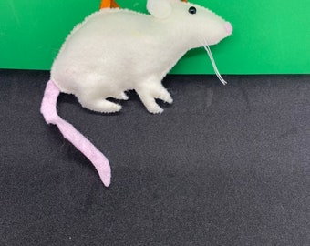 May include: A white felt mouse ornament featuring a pink tail, a small black bead eye, a pink nose, and white thread whiskers. An orange ribbon loop is attached to the top of the mouse's back for hanging, and the edges are finished with visible stitching.