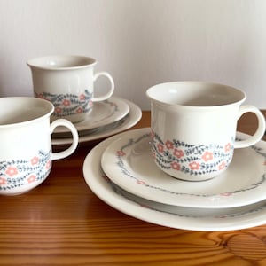 May include: White ceramic teacups and saucers with a floral design. The cups and plates have a blue and pink floral pattern around the rim. The set is displayed on a wooden surface.