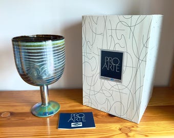 Może przedstawiać: Dekoracyjne kieliszki do wina o unikalnym designie. Kieliszek ma metalowy srebrny trzon i podstawę, z misą, która ma poziome linie i wirujący wzór. Obecne są również pudełko i karta z napisem "PRO ARTE".